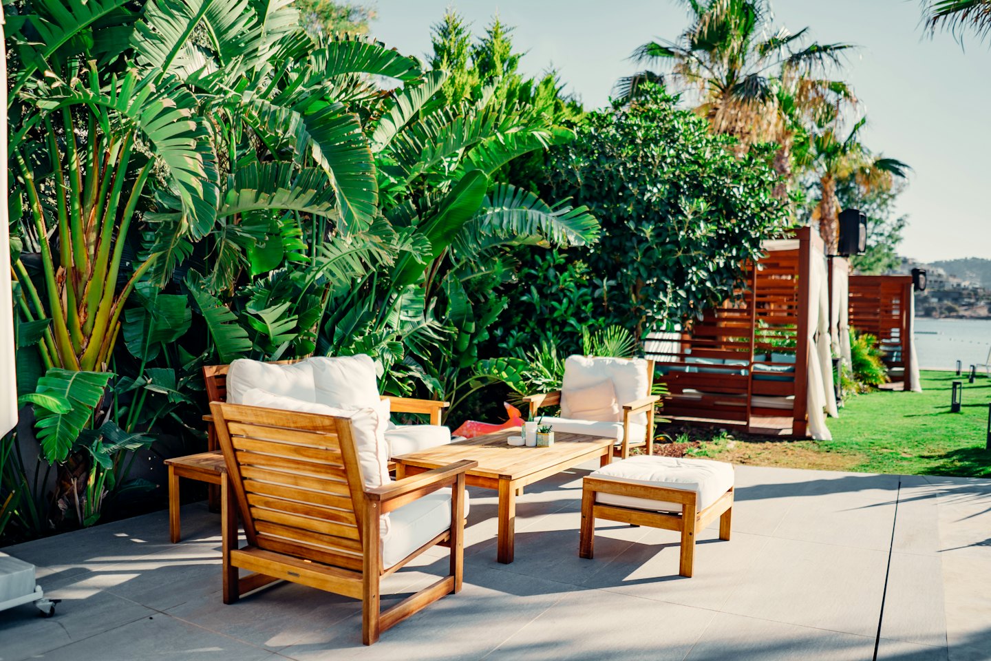 Sillas de madera y mesa de centro en patio embaldosado con plantas tropicales.