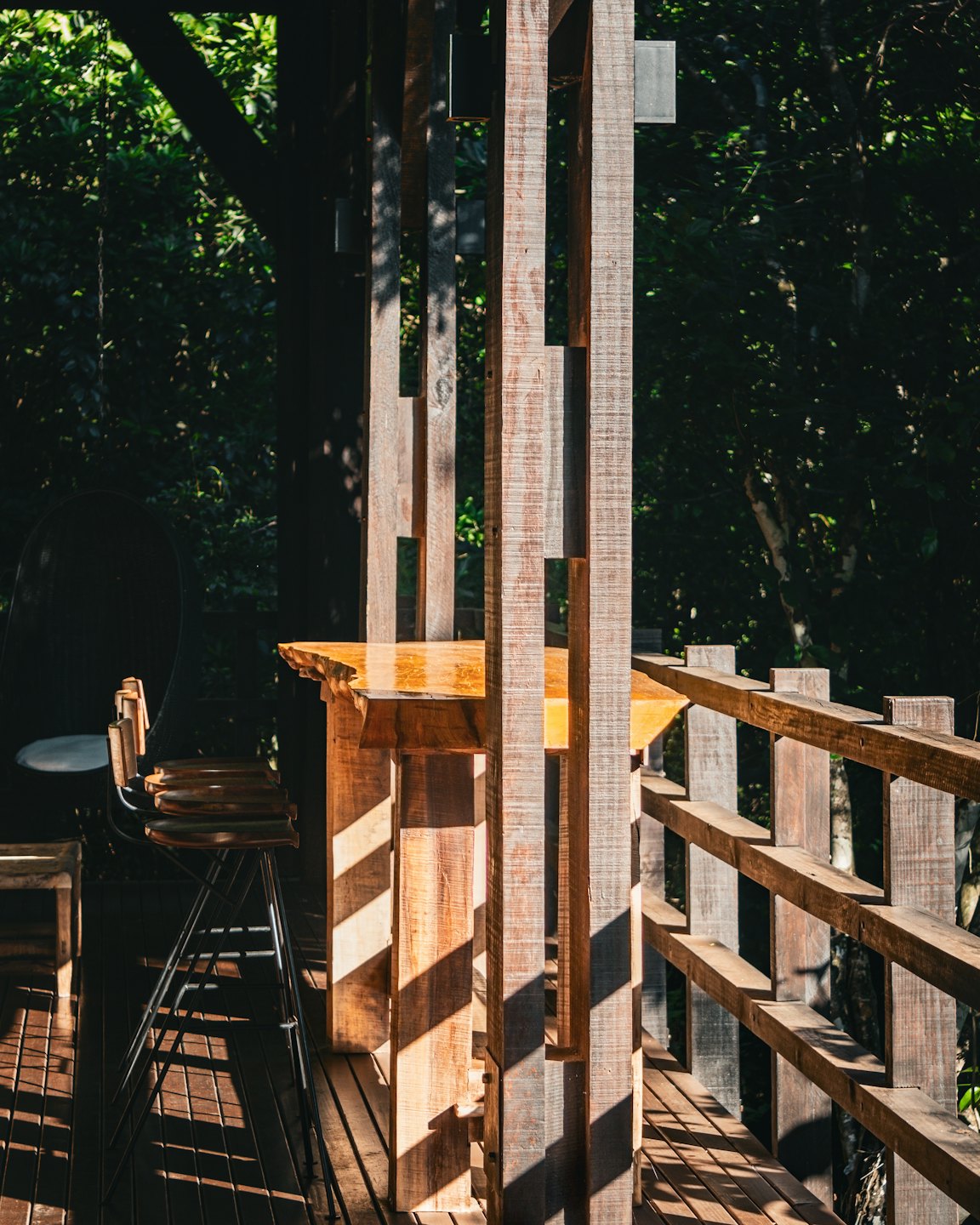 Mesa alta y taburete en una terraza de madera junto a un follaje.