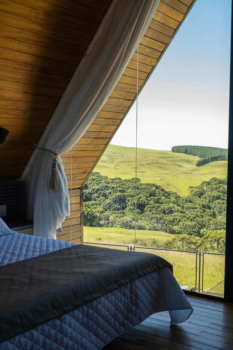 Dormitorio con un gran ventanal triangular con vistas a colinas verdes y bosque.