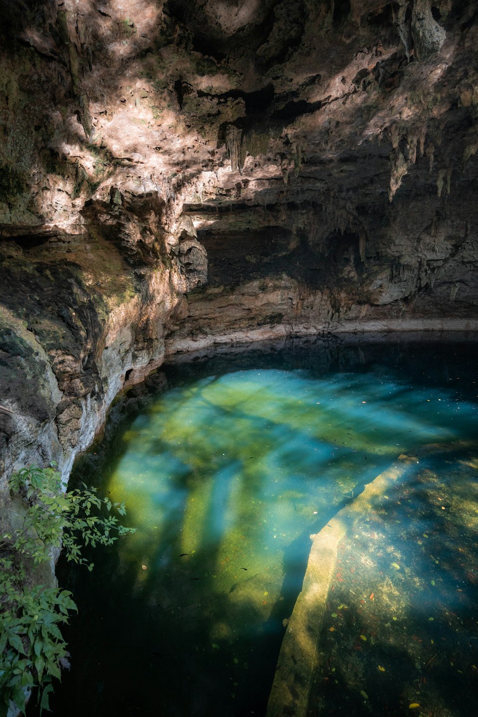 La luz del sol entra en un cenote turquesa rodeado de paredes de piedra.